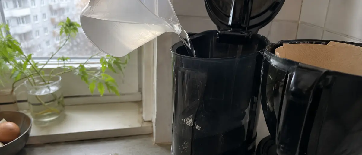 Hand som häller vatten ur en bägare i kaffebryggarens vattentank